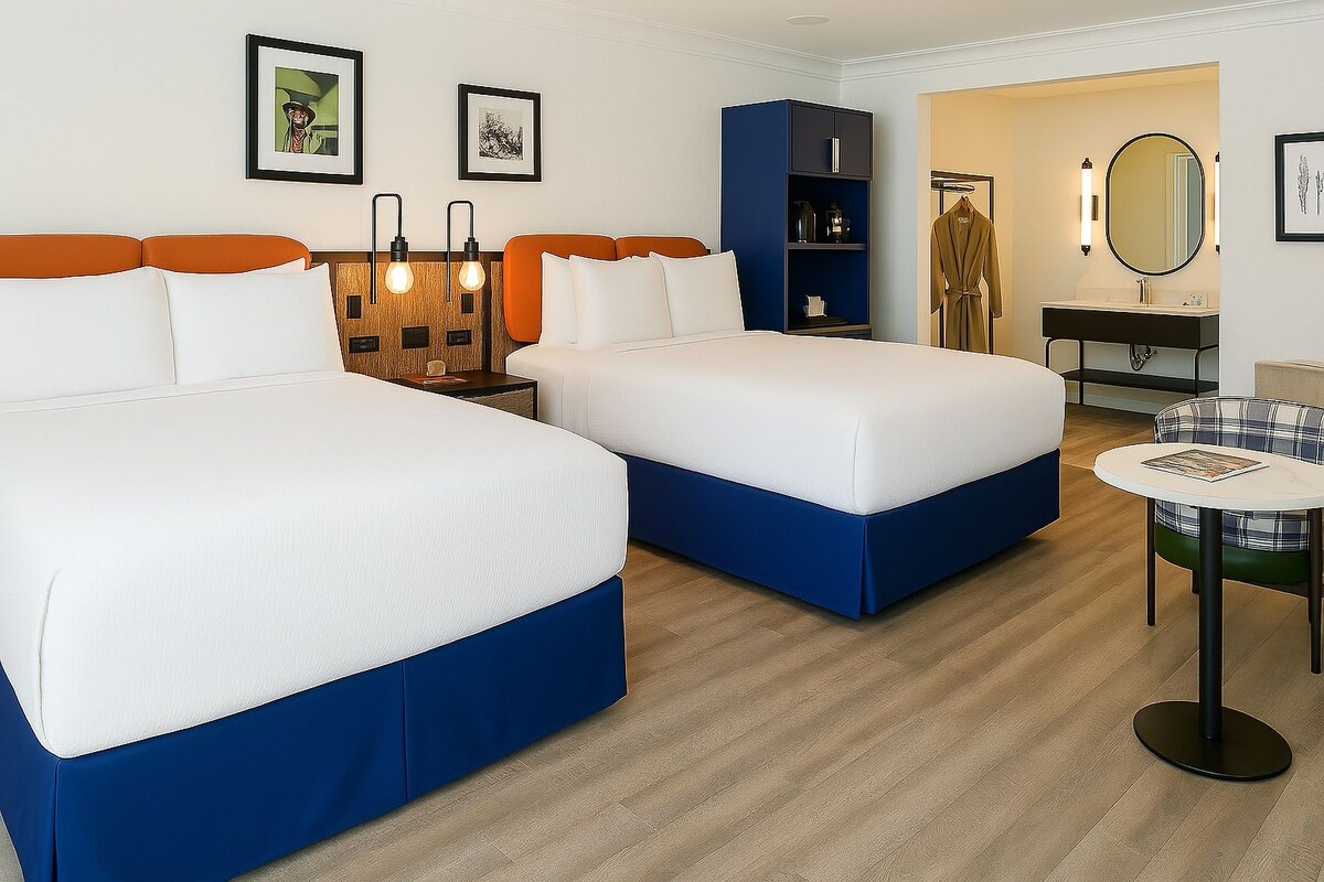 A hotel room with two beds, a small table, a wardrobe, and a bathroom with a mirror.