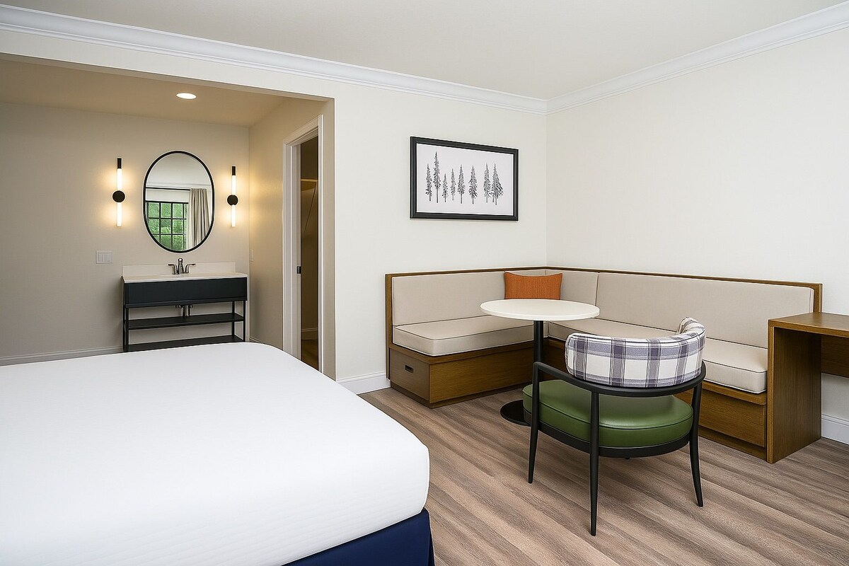 Habitación de hotel con cama, una mesita, un sofá, una banca, un espejo y un cuadro en la pared.