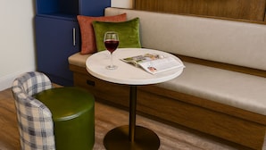 Un rincón acogedor con un sofá, una mesita redonda con una revista y una copa de vino, y un reposapiés verde.