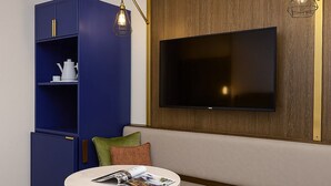 Una habitación moderna con un sofá, una pequeña mesa redonda con revistas, un armario azul y un televisor de pantalla plana montado en una pared de madera.