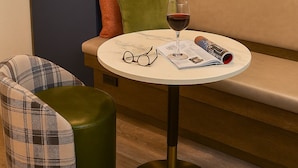 Un rincón acogedor con una mesa redonda, una copa de vino tinto y una revista.