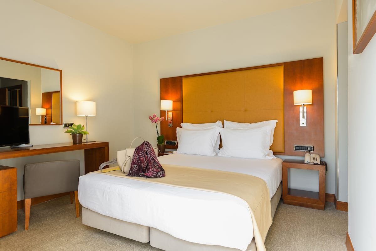 Habitación de hotel con una cama grande, un escritorio con computadora, una silla, un televisor y una mesita de noche con lámpara y teléfono.