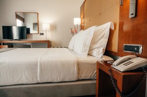 Habitación de hotel con cama, mesita de noche con teléfono, televisión y espejo en la pared.
