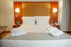 A hotel room with a large bed, two bedside tables, a nightstand, a lamp, and a potted plant.