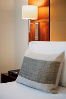 A neatly made bed with a white pillow and a textured pillow. A bedside table with a lamp is visible.