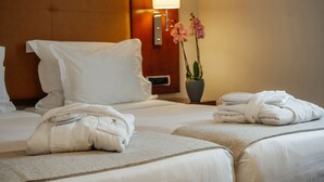 Habitación de hotel con dos camas, una mesita de noche con una lámpara, un jarrón con flores y toallas dobladas sobre las camas.