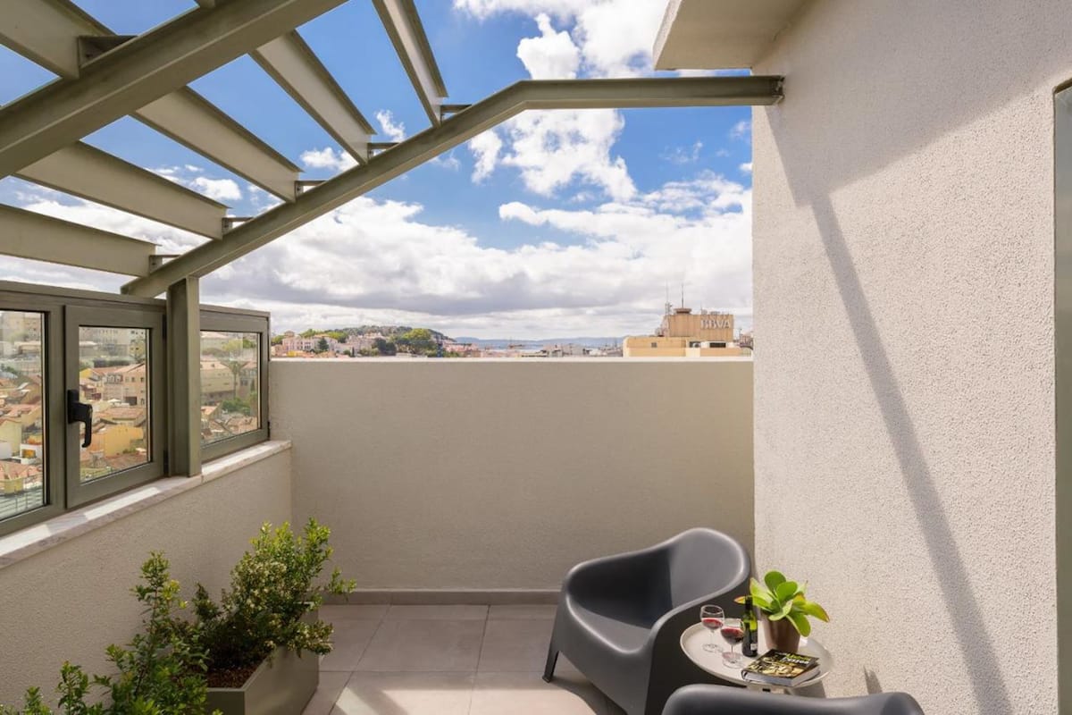 Un balcón con vistas a la ciudad, una mesa con una copa de vino y una planta en maceta.