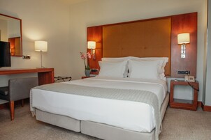Une chambre d’hôtel avec un grand lit, un bureau, une chaise, un miroir et deux lampes de chevet.