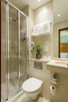 A modern bathroom with a glass shower enclosure, a toilet, a sink with a mirror, and a potted plant.