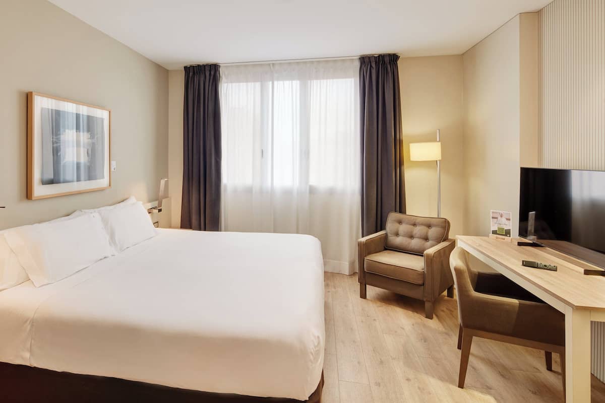 Habitació d'hotel amb un llit gran, una taula amb una cadira, una televisió i un quadre al mur.
