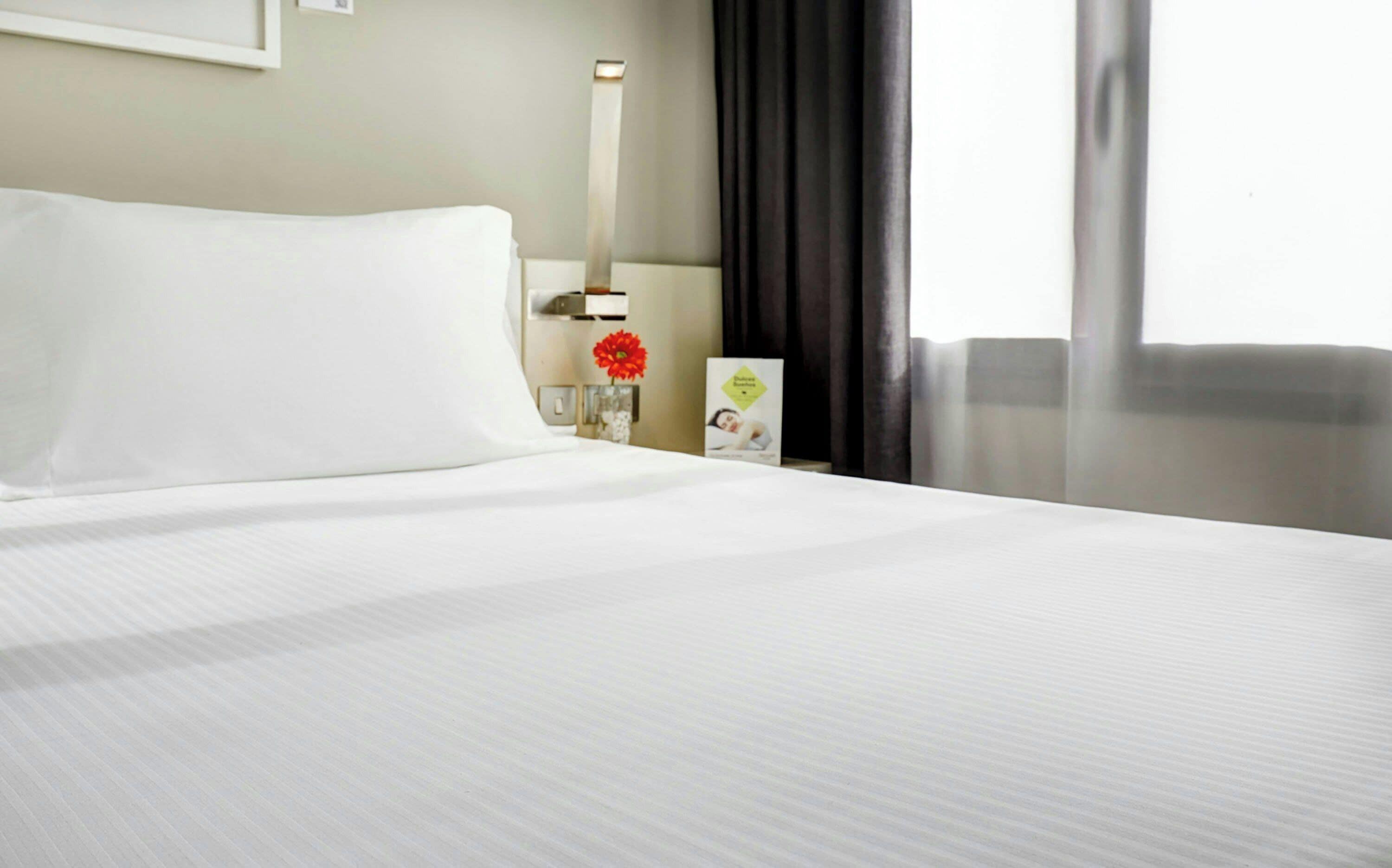 Una habitación de hotel con una cama bien hecha, una mesita de noche con una lámpara, un florero y un cuadro en la pared.