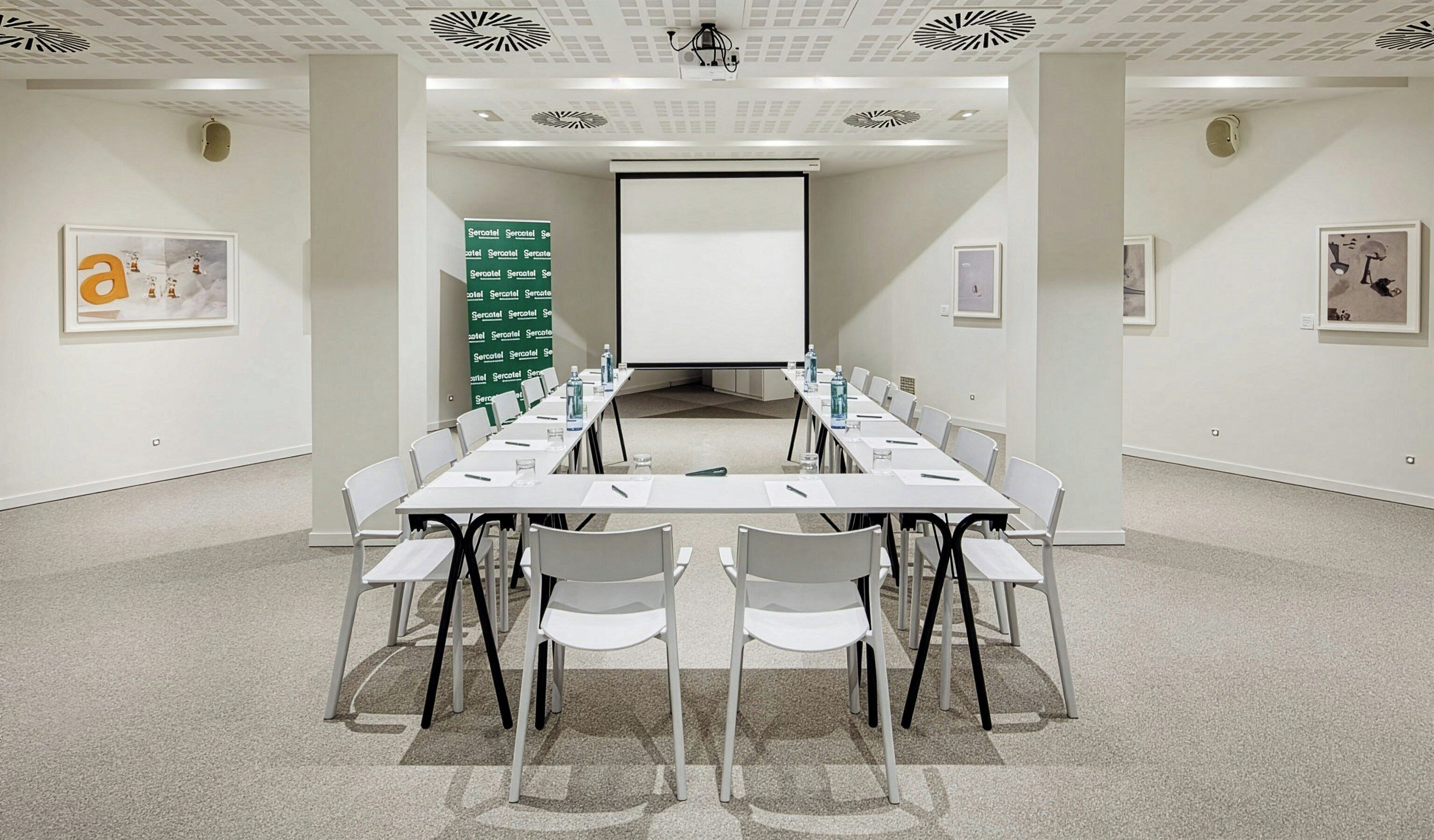 Uma sala de conferências com uma mesa comprida, cadeiras, uma tela de projetor e um quadro branco.