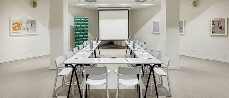 A conference room with a long table, chairs, a projector screen, and a whiteboard.