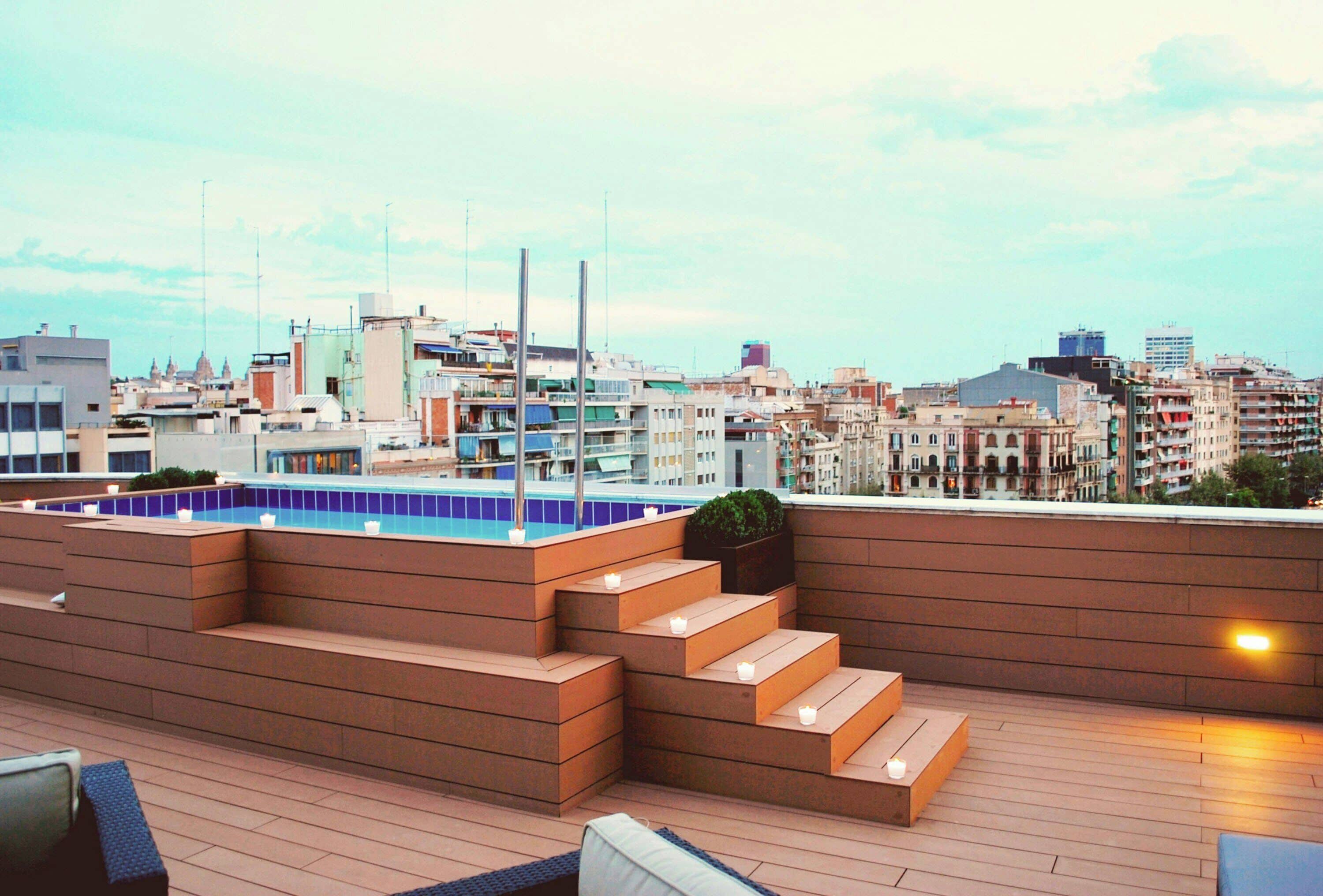 A rooftop terrace with a pool, steps, and seating areas.