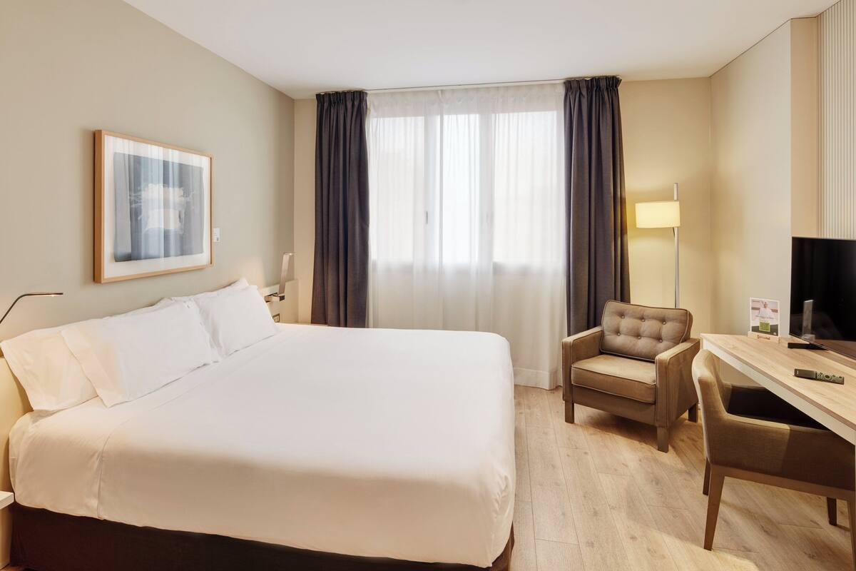 Habitación de hotel con una cama grande, un escritorio con silla, un televisor y un cuadro en la pared.