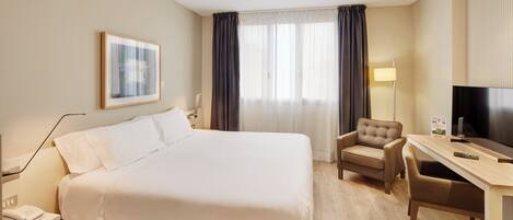 A hotel room with a large bed, a desk with a chair, a television, and a framed picture on the wall.