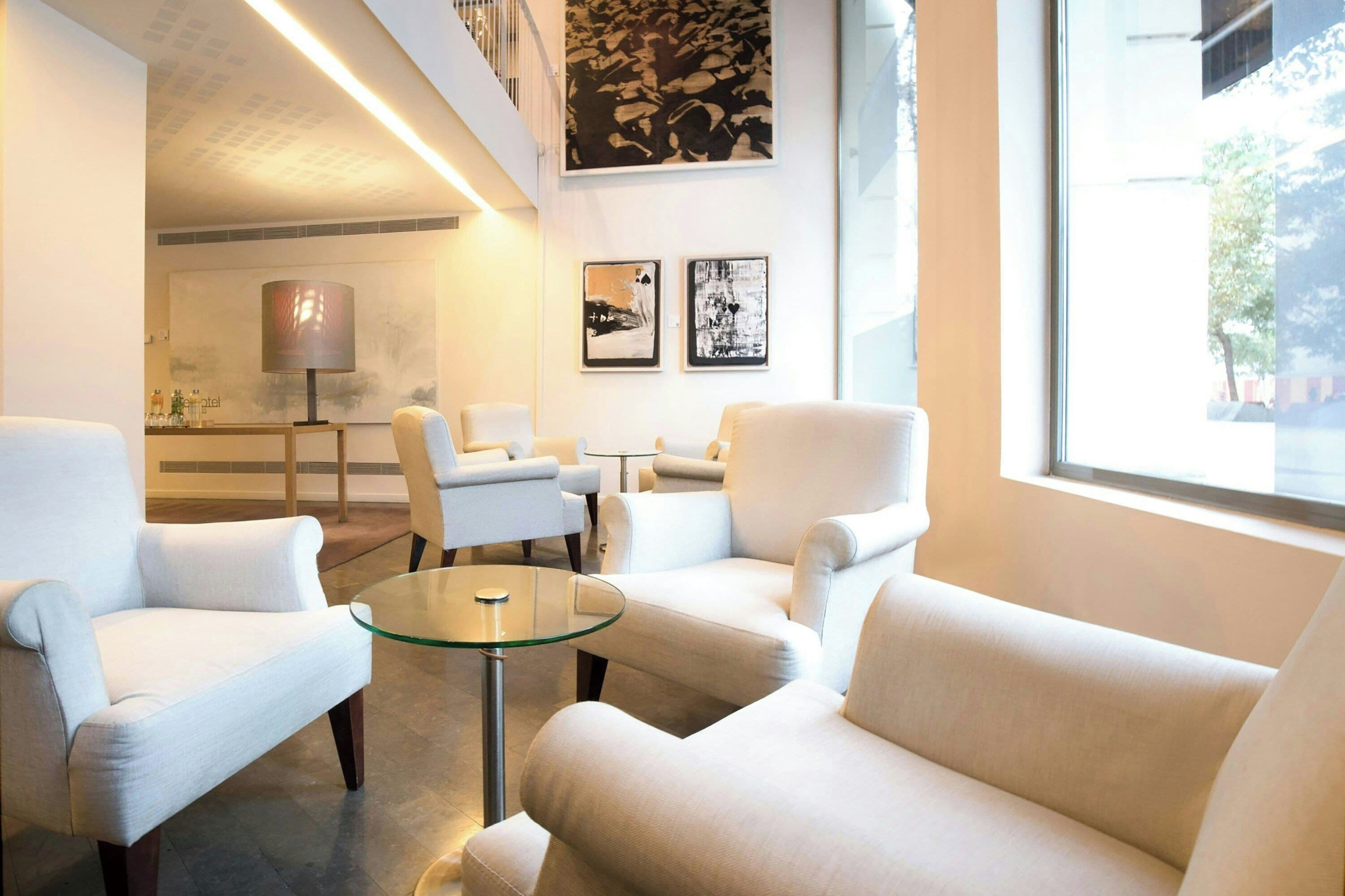 Um lobby de hotel moderno com área de estar, sofás e poltronas, mesa de centro de vidro e obras de arte nas paredes.