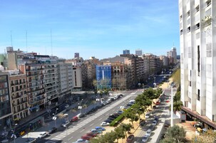 A city street with multi-story buildings, a clear sky, and parked cars.