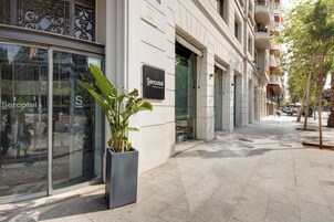 Fachada de hotel com uma grande entrada de vidro, uma placa com a inscrição "Sercotel" e um vaso de planta em primeiro plano.