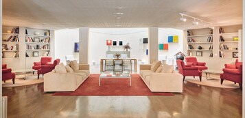 A spacious living room with two beige sofas, red armchairs, and a coffee table. There are bookshelves on both sides filled with books and decorative items.