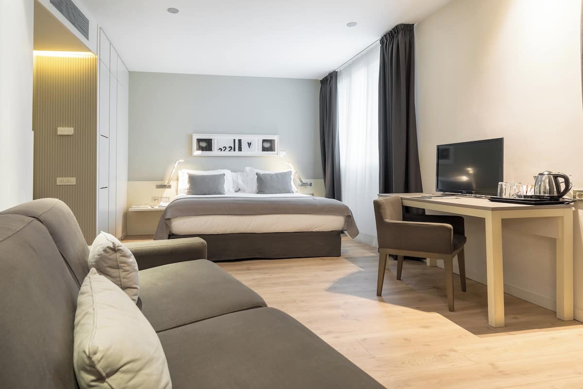 Una habitació d'hotel moderna amb un llit, un escriptori amb un televisor, un sofà i una taula de cafè.