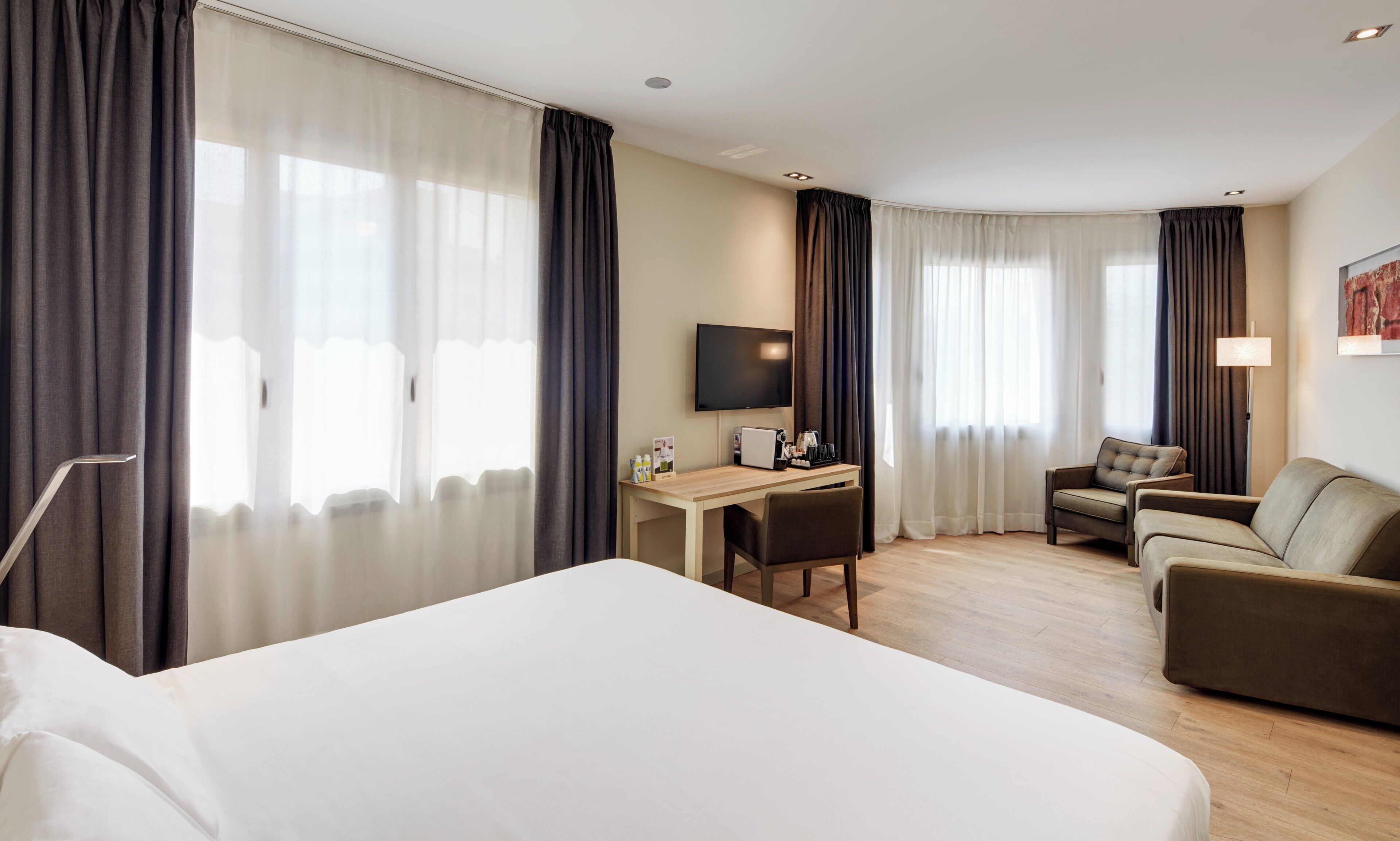 Una habitación de hotel con una cama grande, un escritorio con computadora, un televisor y dos sillones.