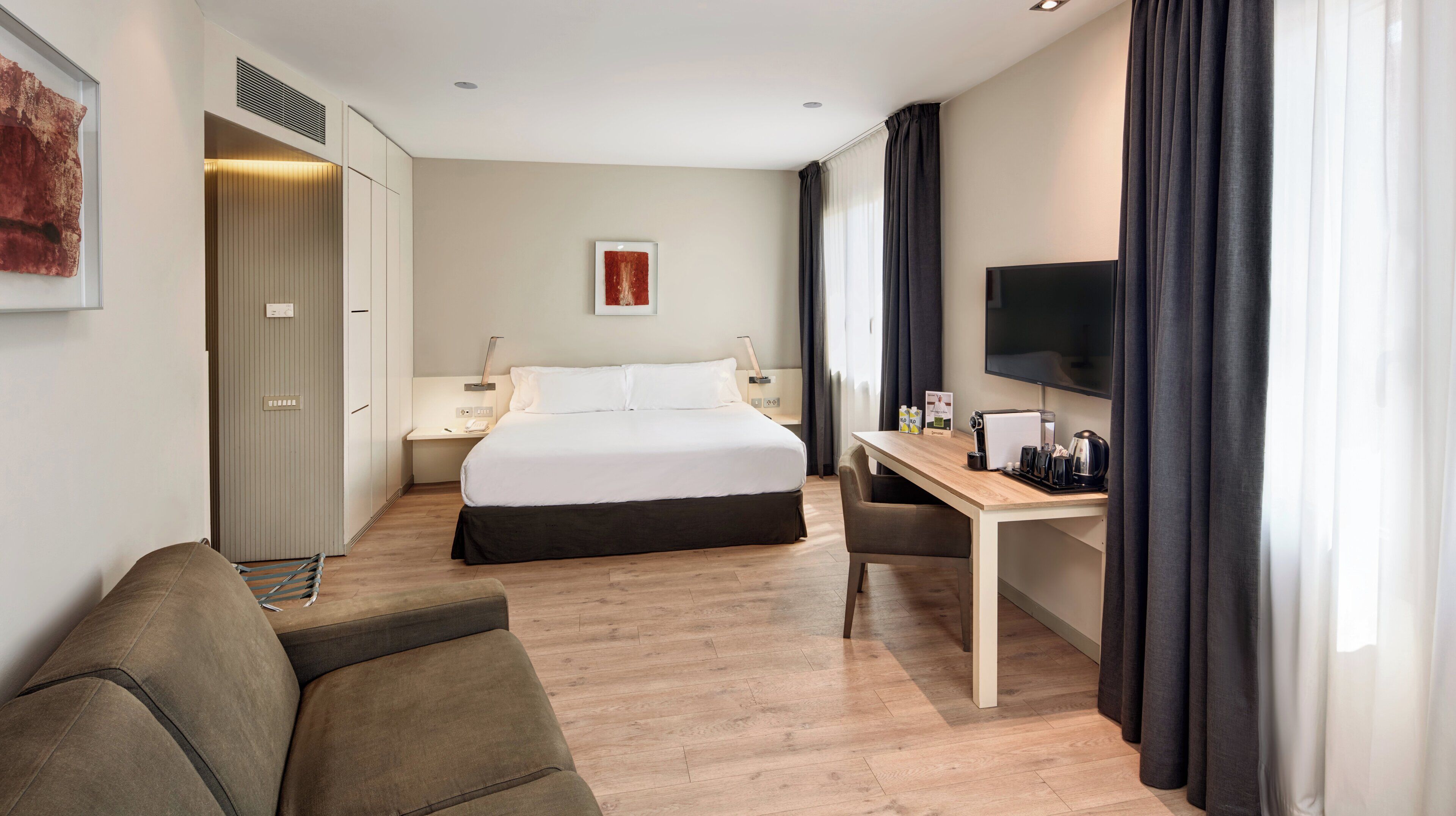 Una habitación de hotel con una cama, un escritorio con una silla, un televisor y un armario.