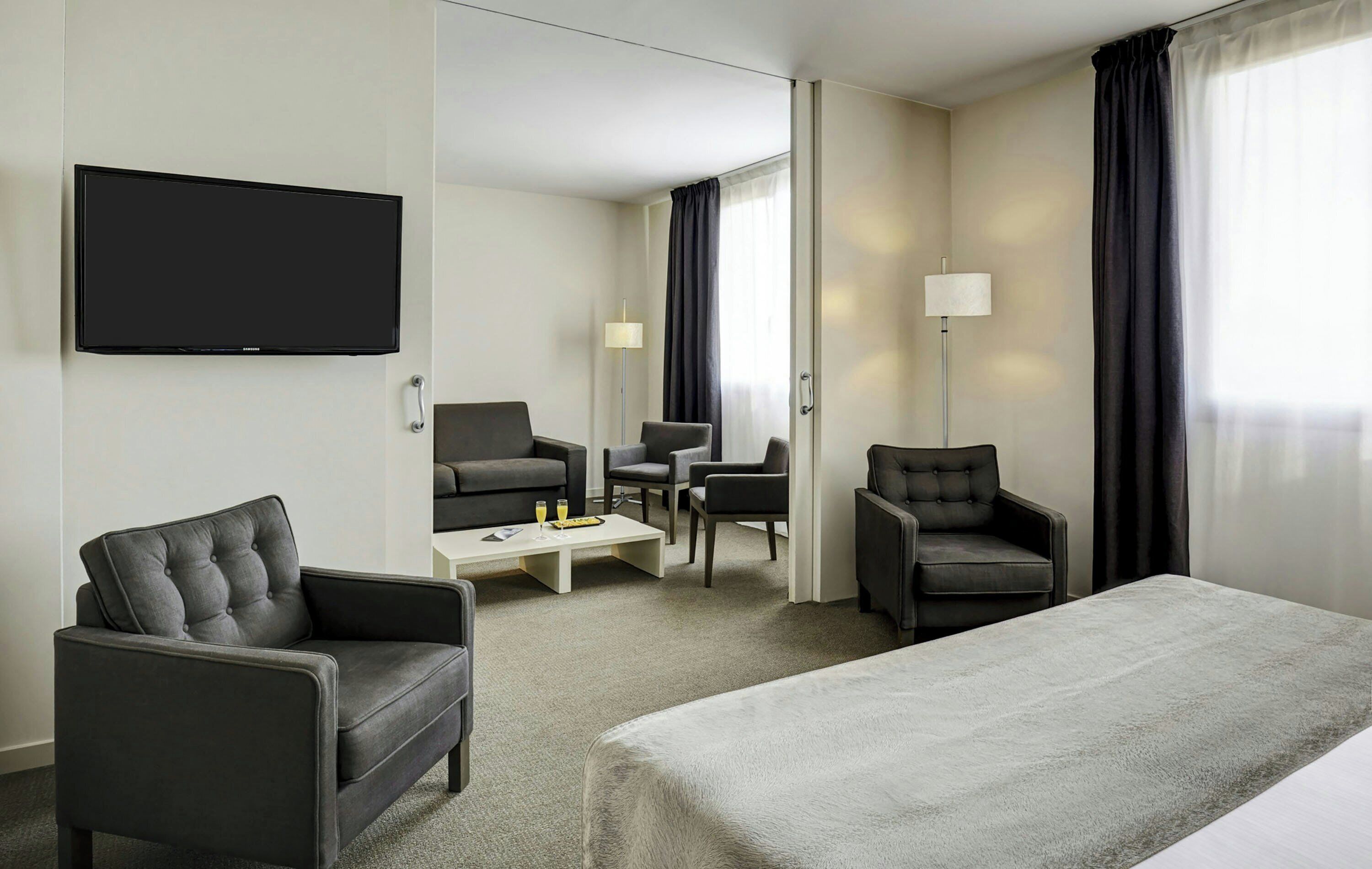Habitación de hotel con cama, dos sillones, una mesa de centro, televisor y puerta que da a un baño.