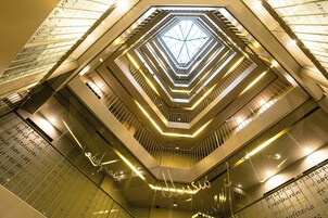 Um átrio com vários níveis, teto com design geométrico e superfícies refletoras.