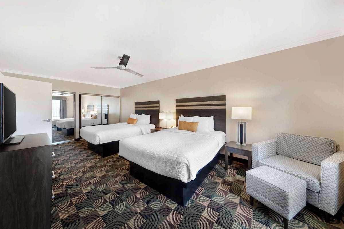 A hotel room with a large bed, two smaller beds, a sofa, a desk with a lamp, and a television.