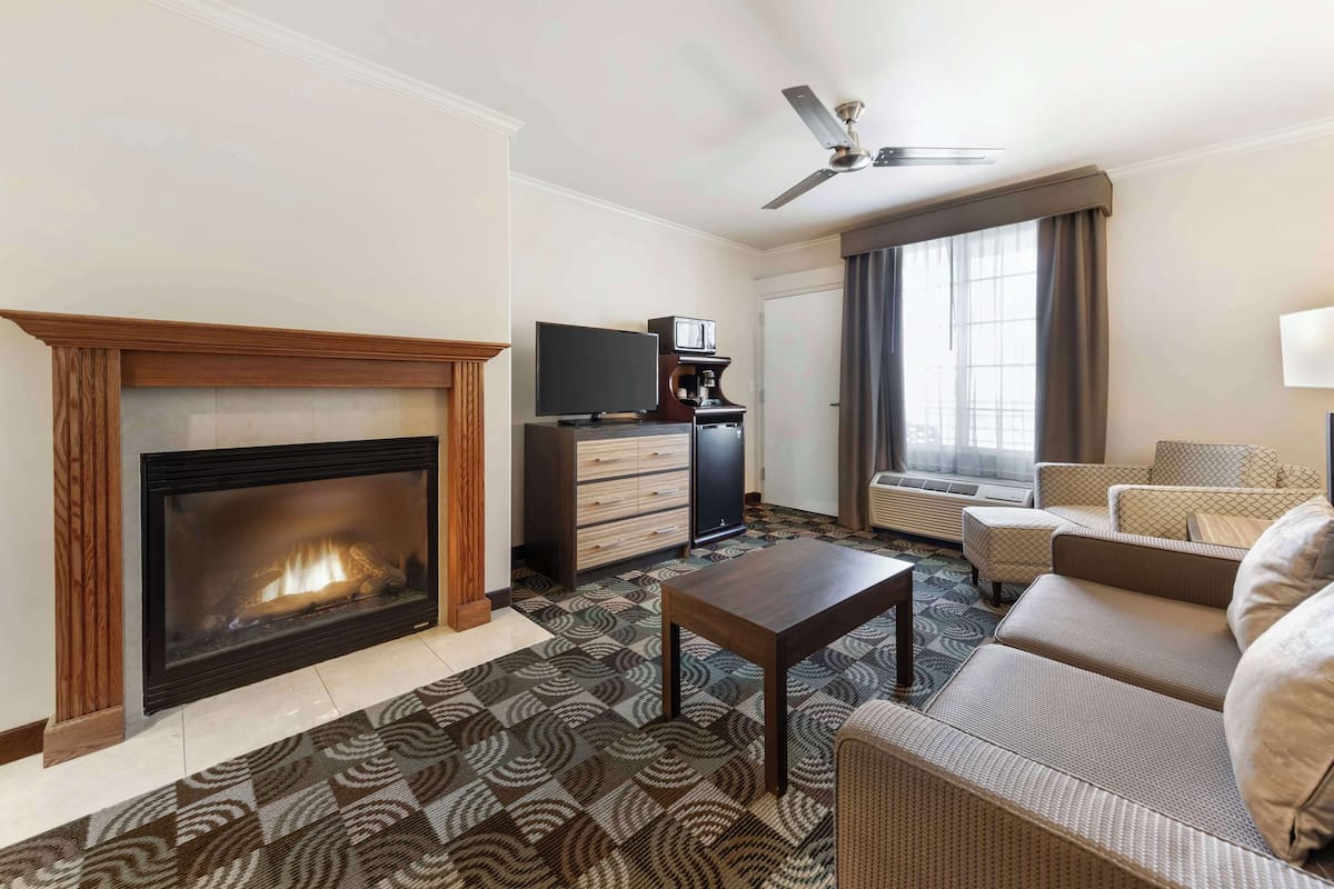A hotel room with a fireplace, a television, a sofa, and a ceiling fan.