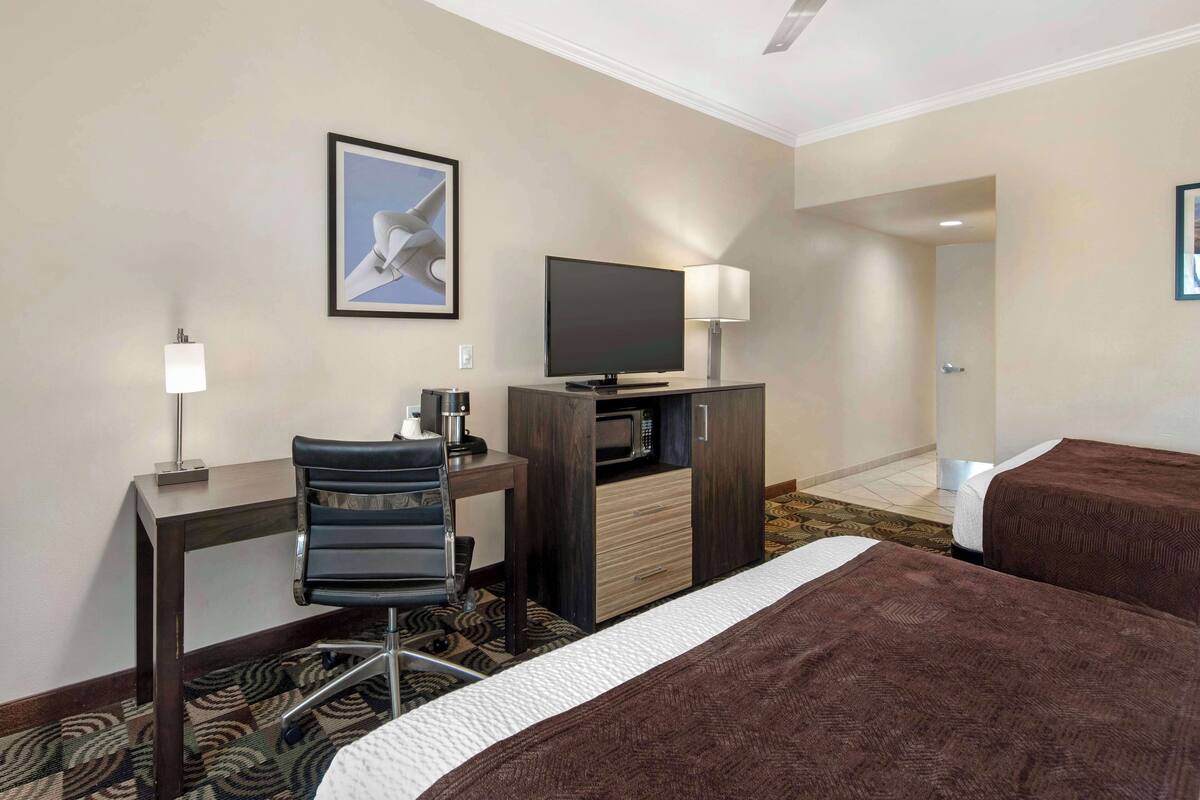 A hotel room with a desk, chair, television, and two beds.