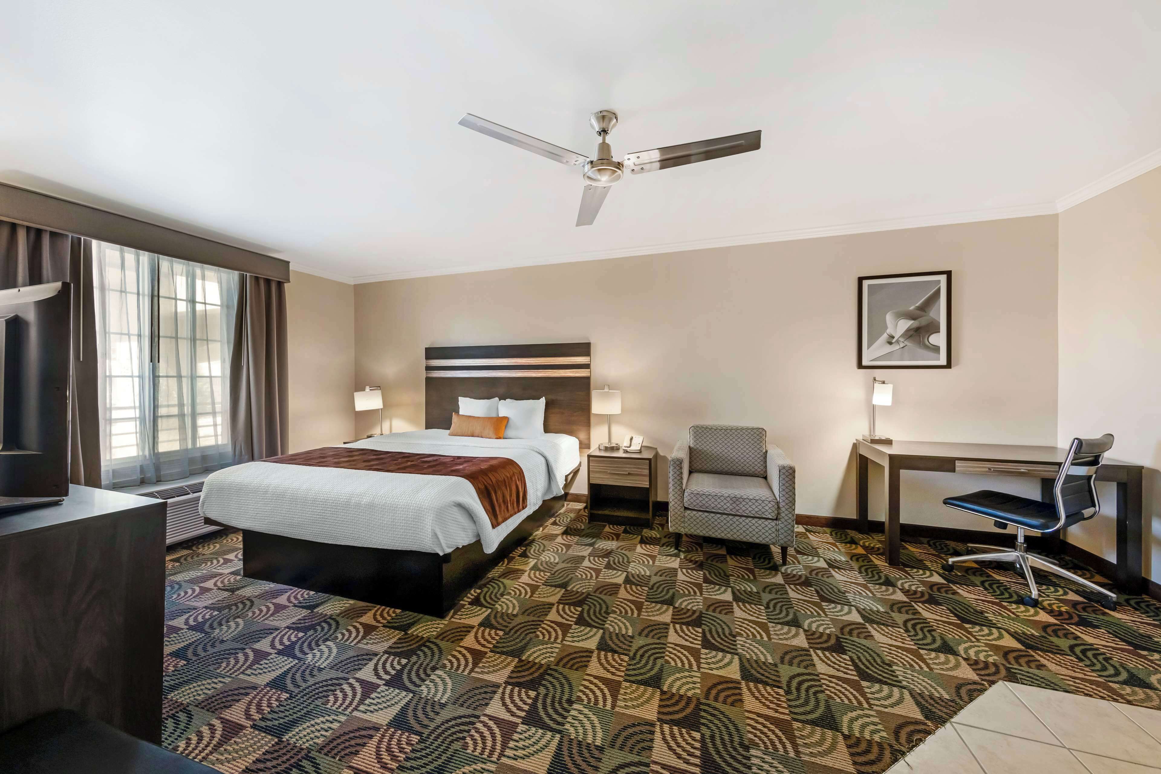 A hotel room with a bed, desk, chair, and a ceiling fan.
