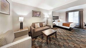 A hotel room with a sofa, a bed, a coffee table, and patterned carpet. - Best Western Plus Country Park Hotel (Tehachapi)