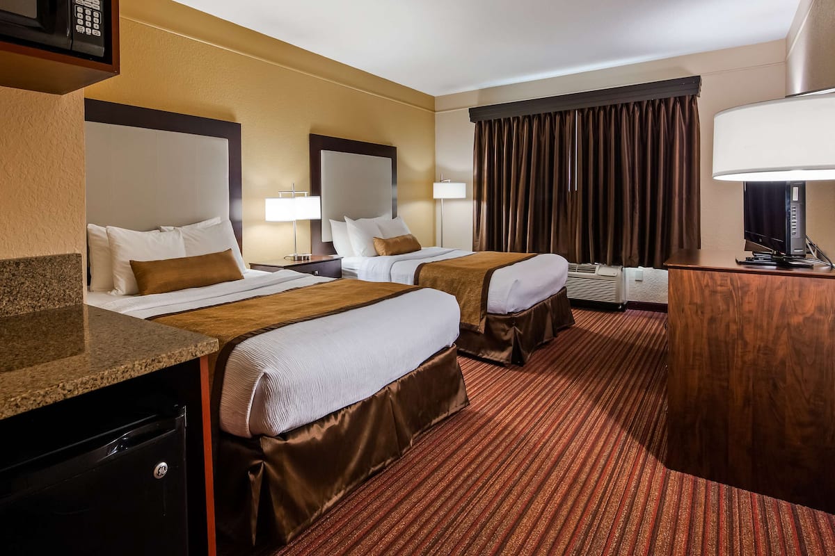 A hotel room with two beds, a desk, a microwave, a lamp, and a television.
