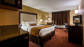 A hotel room with a large bed, a desk with a computer, a television, and a wall-mounted air conditioning unit.