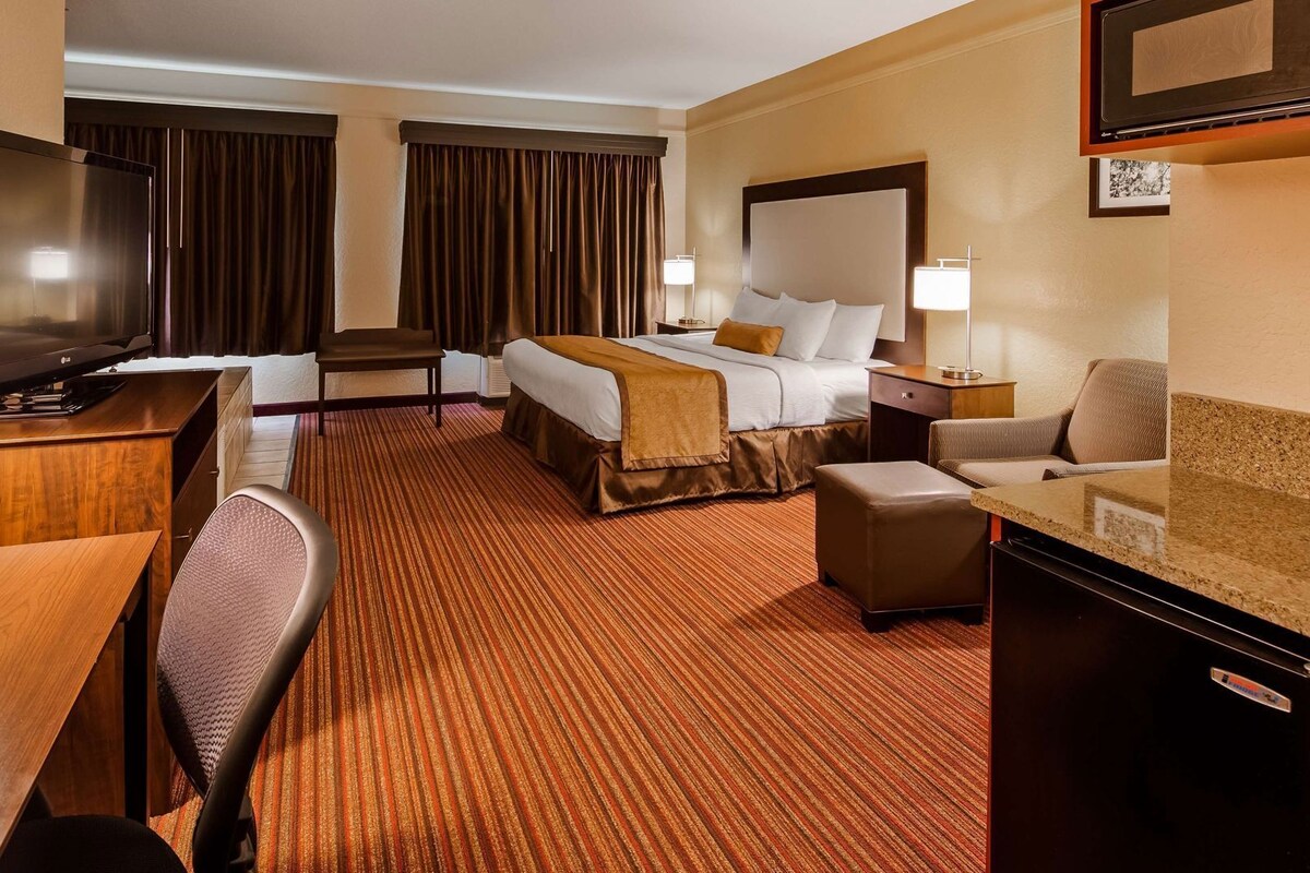 A hotel room with a bed, desk, chair, TV, and a minibar.