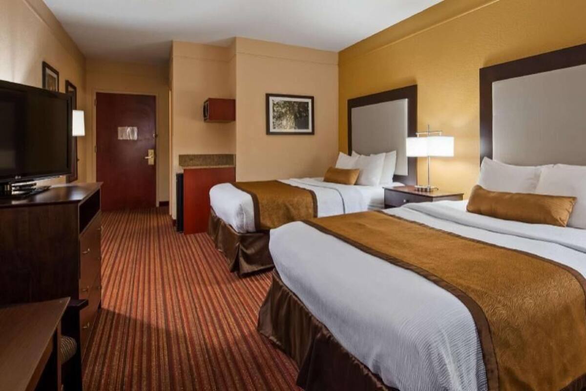 A hotel room with two beds, a television, a desk, and a door.