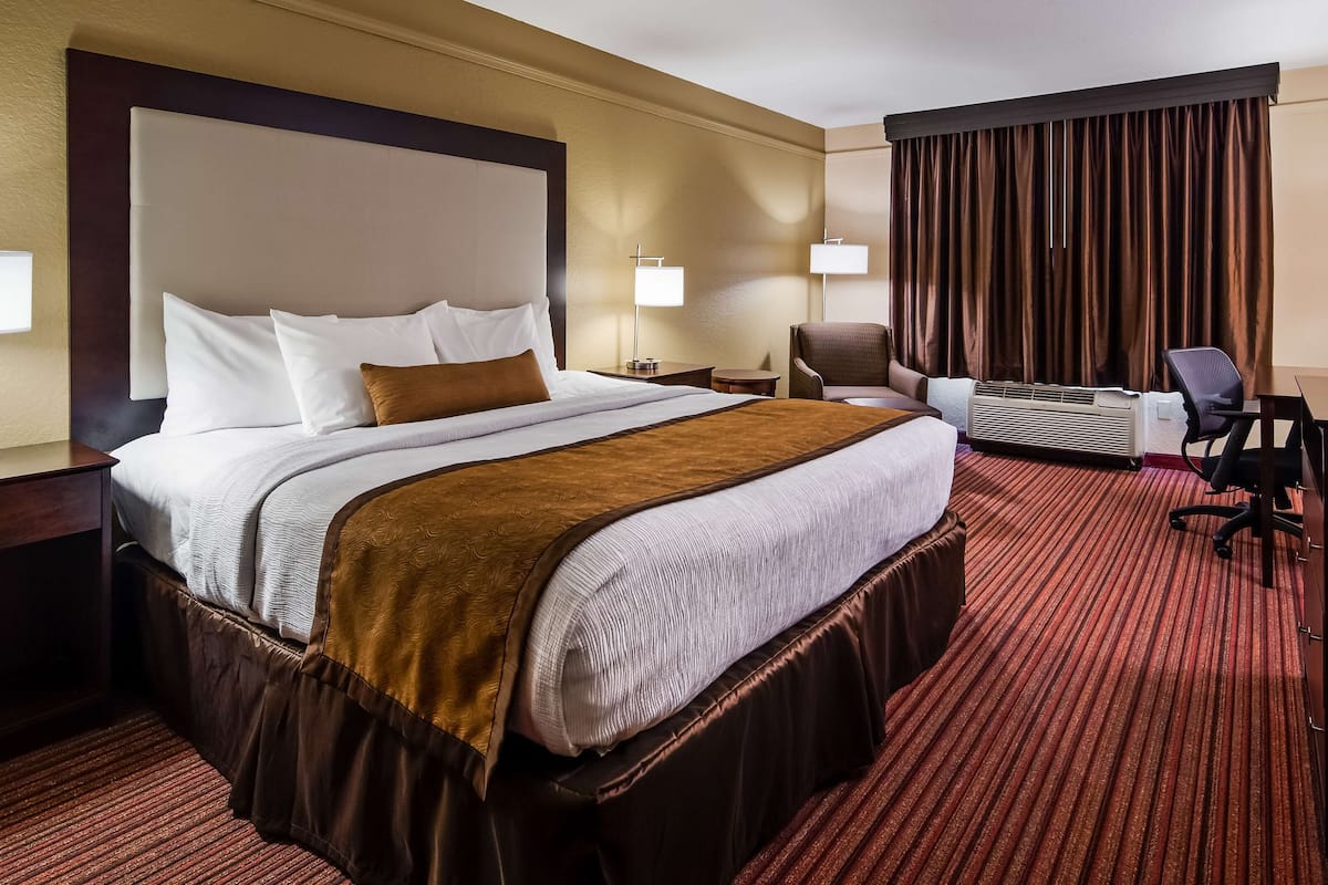 A hotel room with a large bed, a desk, a chair, a television, and a window with curtains.