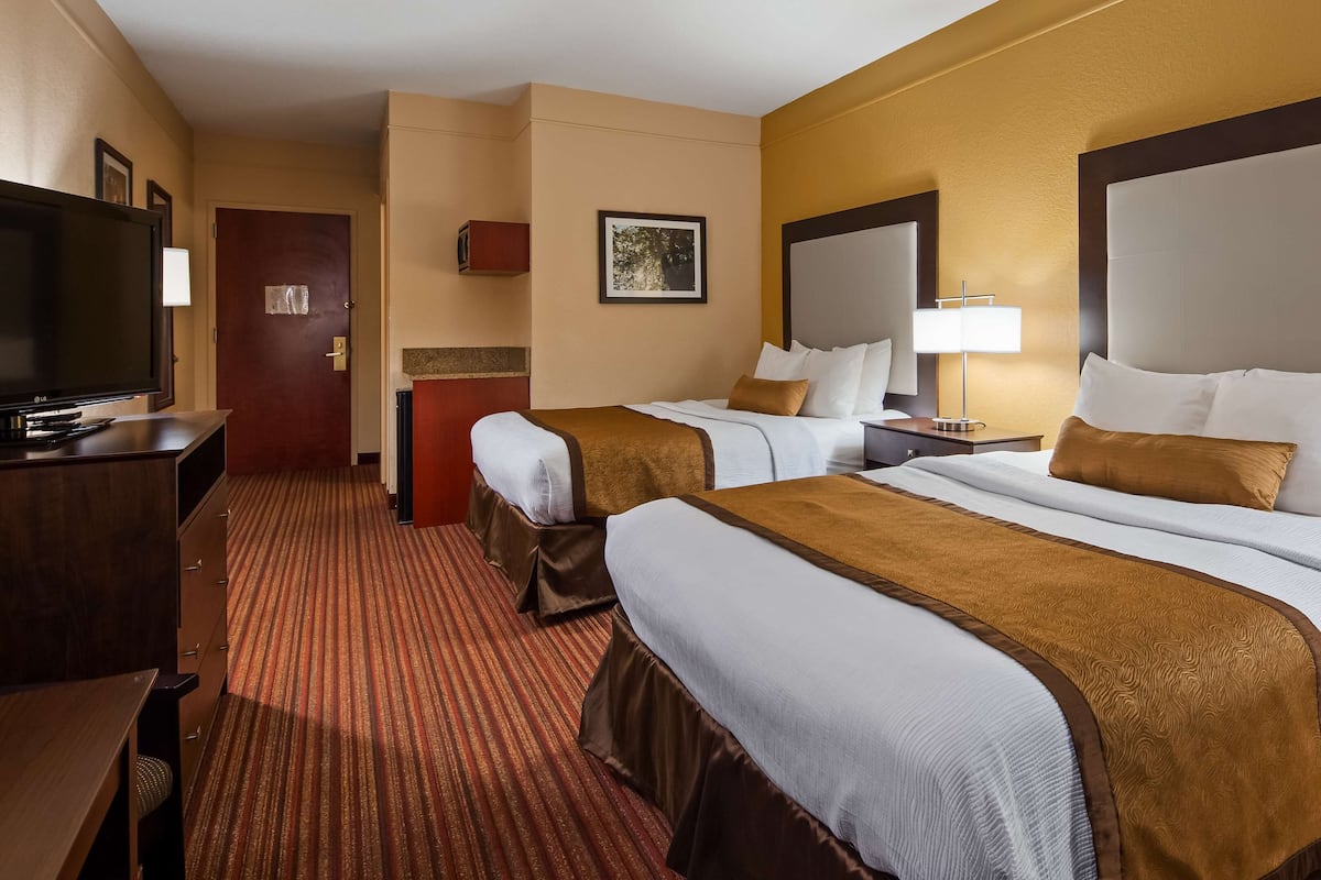 A hotel room with two beds, a TV, a desk, and a carpeted floor.