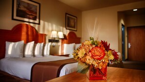 A hotel room with a bed, a nightstand, and a vase of flowers on a wooden table.