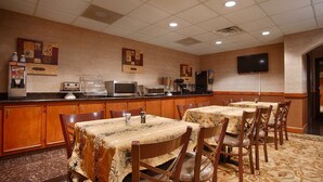 A hotel dining area with wooden cabinets, a buffet station, and a flat-screen TV on the wall.