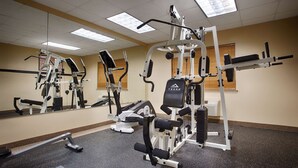 A gym with various exercise machines, mirrors, and a ceiling with fluorescent lights.