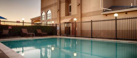 A swimming pool with lounge chairs and a fence.