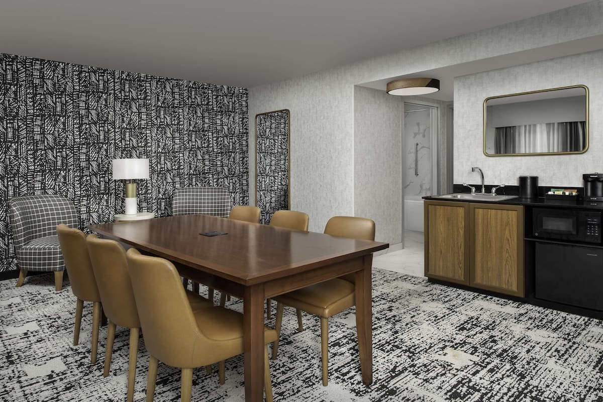 Una habitación de hotel moderna con zona de comedor, kitchenette y papel tapiz estampado.