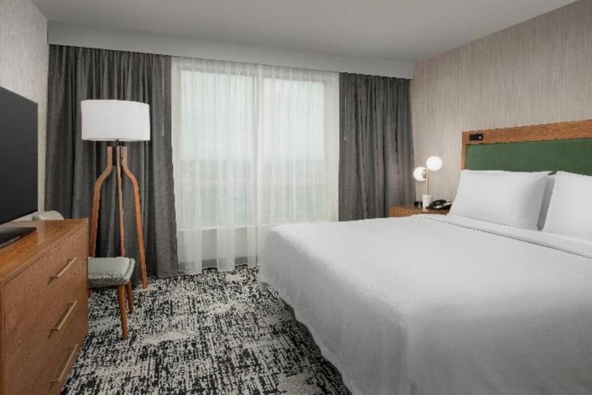 Una habitación de hotel con cama, escritorio, silla, lámpara y mesita de noche.
