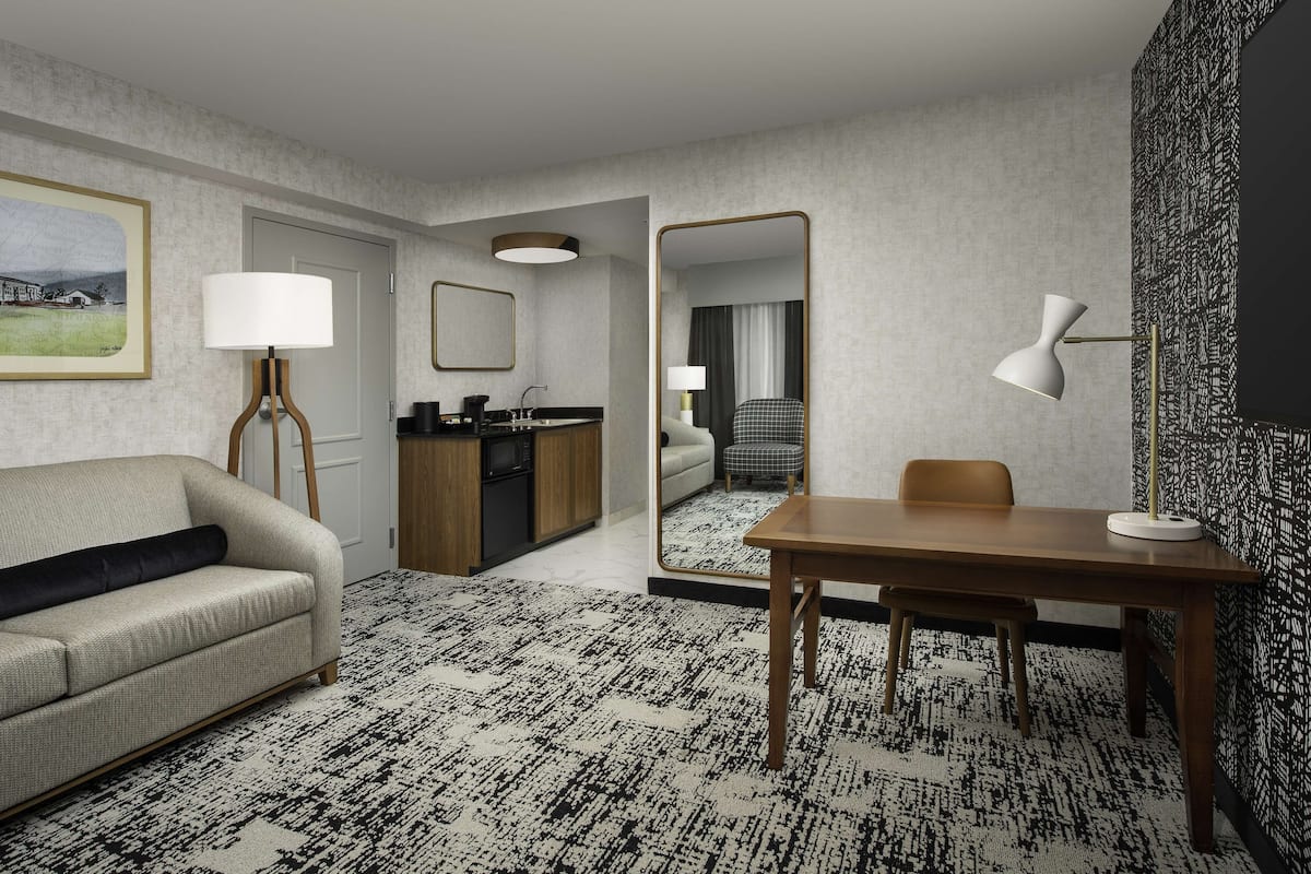 Habitación de hotel con sofá, mesa de comedor, zona de cocina y un espejo grande.