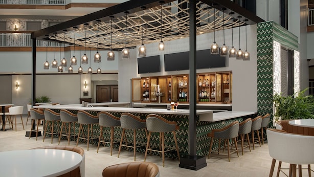 Uma área de bar moderna com teto alto, luminárias pendentes e balcão com banquetas.