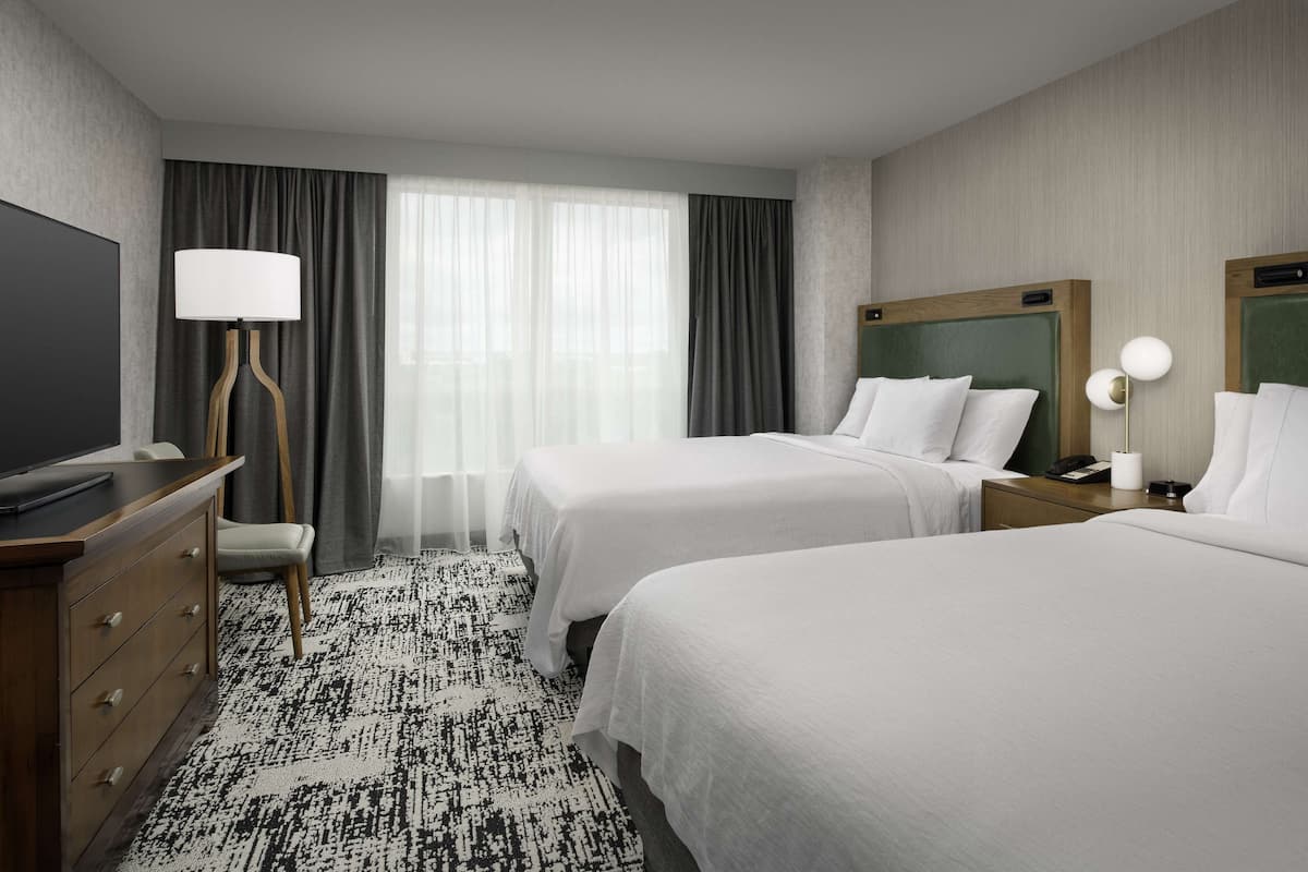 Habitación de hotel con dos camas, un televisor de pantalla plana, un escritorio con lámpara y una alfombra estampada.
