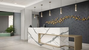 Balcão de recepção com design em mármore, parede escura com detalhes dourados decorativos e luminárias pendentes.